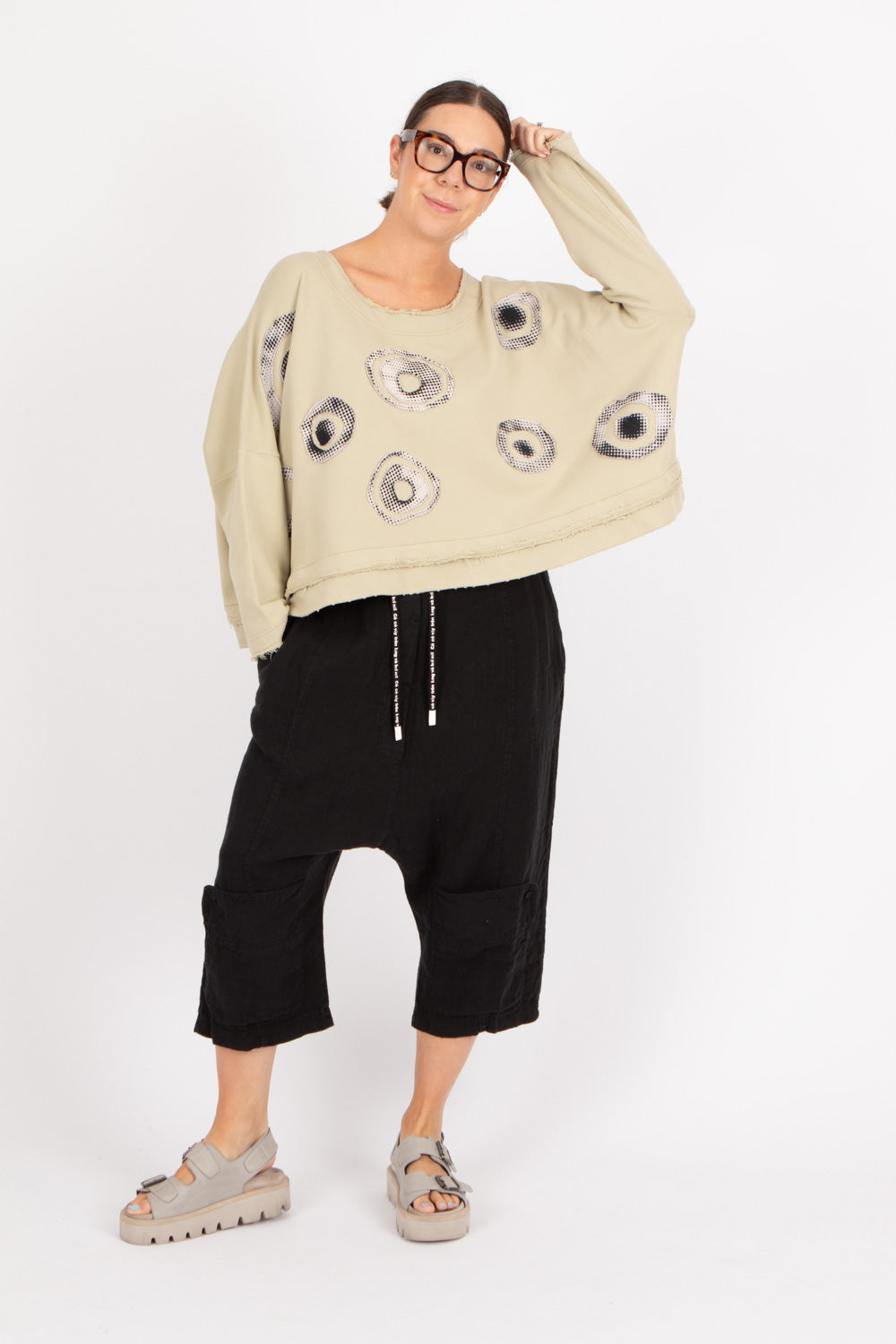 Person wearing a beige sweater with black floral patterns and black pants on a white background