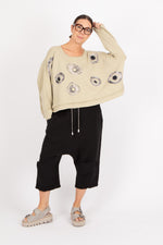 Person wearing a beige sweater with black floral patterns and black pants on a white background