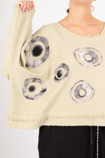 Beige sweater with circular patterns worn by a person on a light gray background